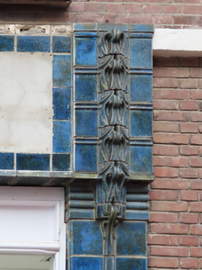 851094 Detail van het blauwe tegelwerk op de pui van het winkelhoekpand Burgemeester Reigerstraat 44 in de ...